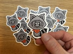 a hand is holding a sticker with several raccoons on it, all in grey and orange