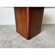 a close up of a wooden table on concrete floor with white wall in the background