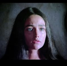 a woman with long hair and blue eyes stares at the camera while standing in front of a wall