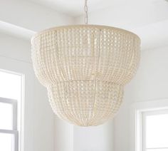 a white chandelier hanging from the ceiling in a room with two windows and a table