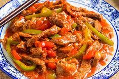 a blue and white plate topped with meat and peppers next to two chopsticks