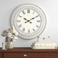 a white clock sitting on top of a wooden dresser next to a vase with flowers