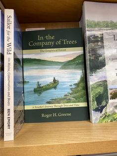 three books are sitting on a shelf in a bookcase, one is titled in the company of trees