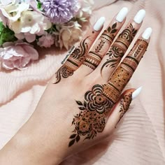 a woman's hand with henna tattoos on it and flowers in the background