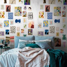 a bed with blue sheets and pillows in front of a wall covered with colorful pictures