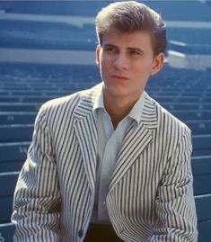 a man in a striped jacket and tie sitting on a bleachers seat looking at the camera