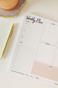 a desk with a planner, pen and cup on it next to an orange vase