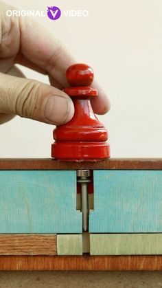 a hand is holding a red object on top of a piece of wood and it's magnets