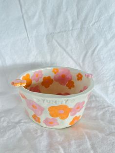 a flowered bowl with a spoon in it on a white tablecloth covered surface