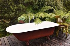 an old fashioned bathtub on a wooden deck with ferns in the background and two chairs