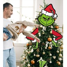 a man holding a baby in front of a christmas tree with the grin face on it