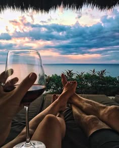 two people sitting on a couch with their feet propped up next to a glass of wine