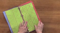 a person is holding a binder on top of a wooden table with a green and blue cover