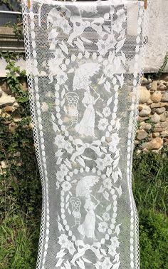 a white crocheted net hanging on a clothes line in front of a stone wall