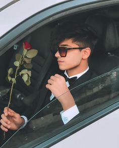 a young man in a tuxedo holding a rose and looking out the window