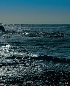 a person walking on the beach with a surfboard in their hand and water splashing around them