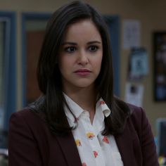 a woman in a white shirt and maroon blazer is looking at the camera with her hands on her hips