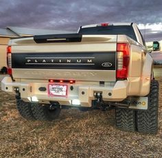 the rear end of a white truck parked on top of a dry grass covered field