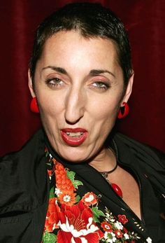 a woman making a funny face while wearing red earrings and a black shirt with flowers on it