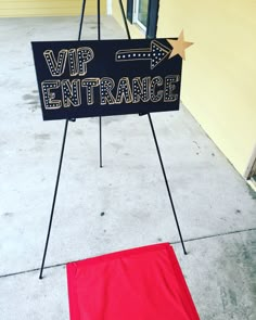 a sign that is on the sidewalk with a red carpet in front of it and a yellow building behind it