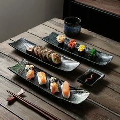 three black plates with sushi and chopsticks on a wooden table