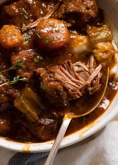 a white bowl filled with meat and potatoes covered in gravy, garnished with parsley