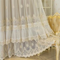 a chair and curtain in front of a window with white lace on the curtains,