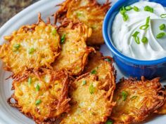 potato cakes with sour cream and chives on a white plate next to a blue bowl