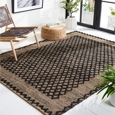 a black and tan rug with geometric design on the floor next to a chair, potted plant and framed pictures