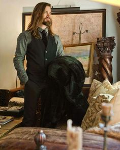 a man with long hair wearing a suit and tie standing in front of a painting