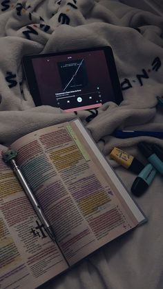 an open book on a bed next to a cell phone and pen with the screen turned off