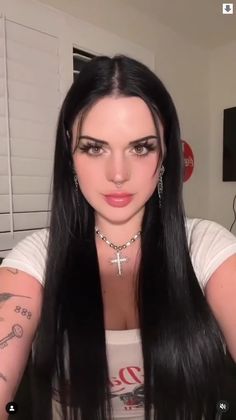 a woman with long black hair and piercings on her chest is looking at the camera