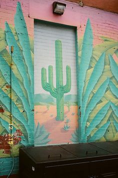 a mural on the side of a building with cactus and leaves painted on it's walls