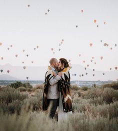 a man and woman standing in the middle of a field with balloons flying above them