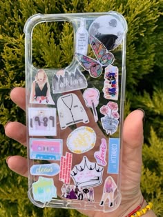 a person holding up a clear case with stickers on it's side and various things in the back