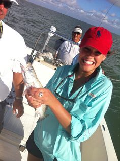 a woman holding a fish while standing on a boat with two men in the background