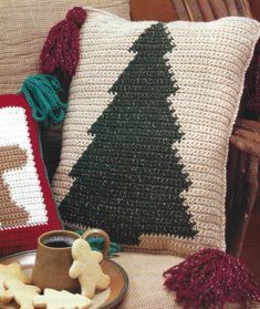 a crocheted christmas tree pillow on a chair next to a cup of coffee