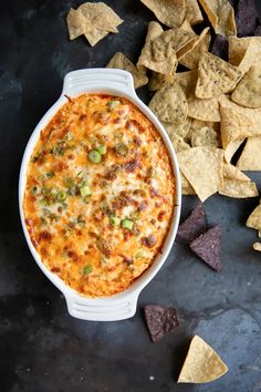 a white bowl filled with cheese and vegetables next to tortilla chips on a black surface