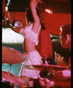 a woman in a pink dress is playing drums on stage with other people behind her