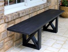 a wooden bench sitting in front of a window on top of a stone floor next to a potted plant