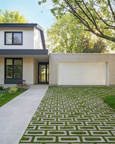 a modern house with grass in the front yard and landscaping on the side walk leading up to it