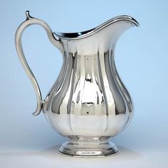 a silver pitcher sitting on top of a white table next to a light blue wall