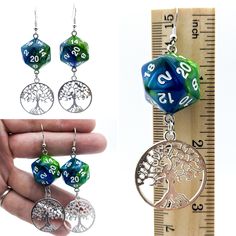 a pair of green and blue earrings with tree of life charms hanging from them next to a ruler