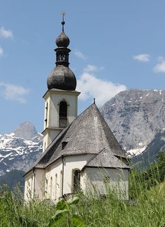 an old church sits in the middle of tall grass with mountains in the back ground