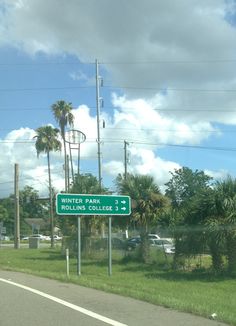 a street sign on the side of a road in front of palm trees and clouds