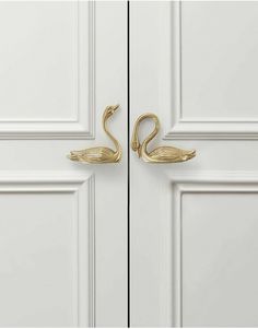 two brass swan hooks on the side of a white door