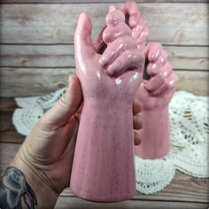 a hand holding a pink ceramic object on top of a table