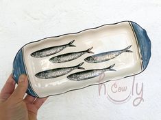 a hand holding a plate with fish on it and the bottom is painted in blue