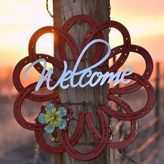 a welcome sign hanging from a wooden pole with a flower in the center and an open circle around it