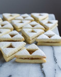 several pieces of powdered sugar covered cookies on a marble counter top with one cut in half to show the filling